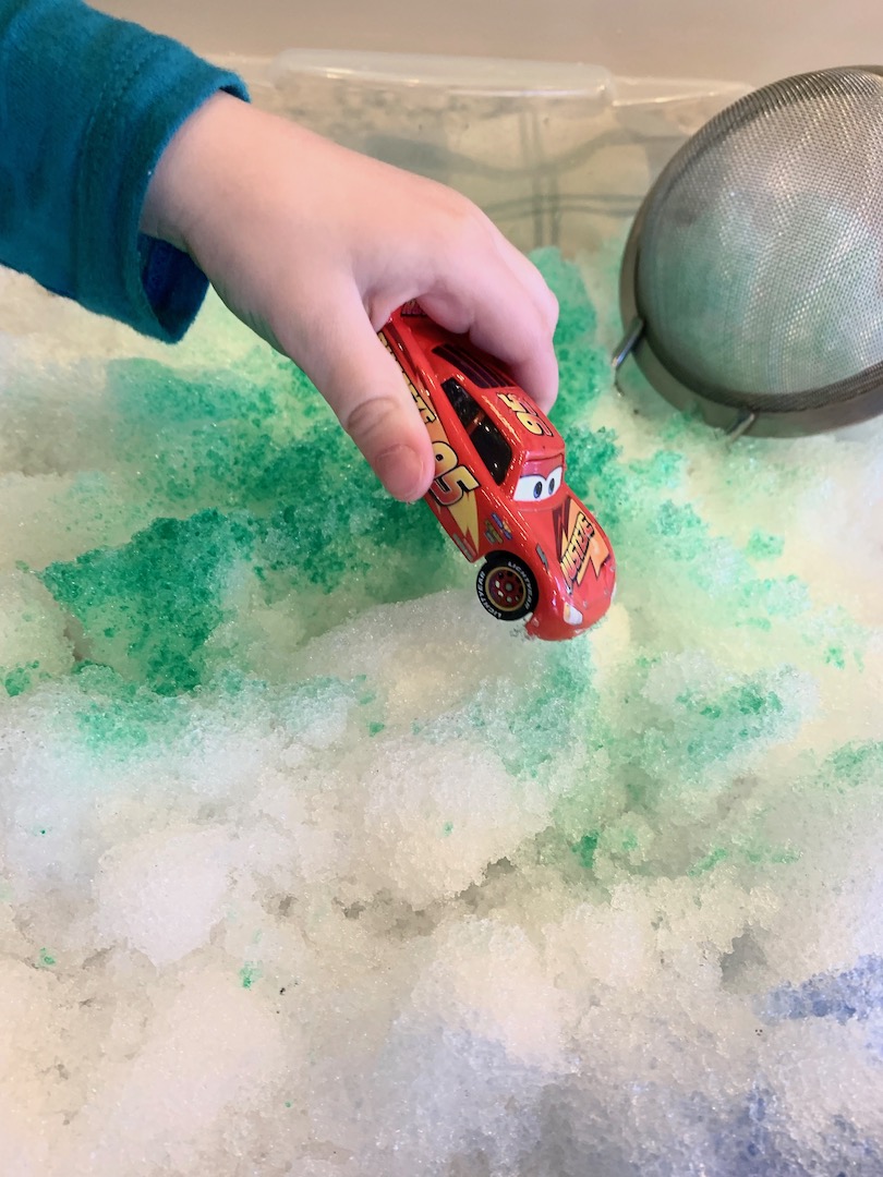 Lightning McQueen car in child's hand as he plays in snow colored green and purple