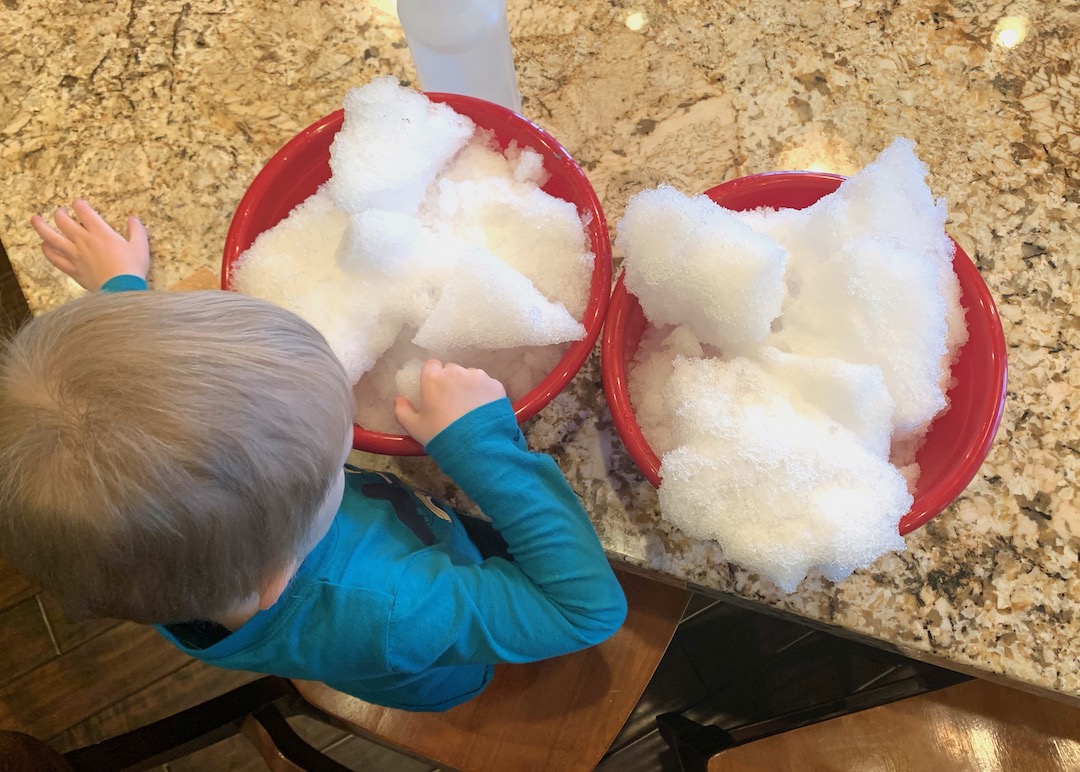 overhead view of child with snow sensory bin supplies - two red bowls filled with snow