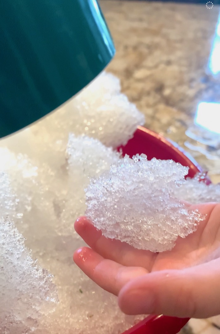 child holding melting snow while blow dryer melts snow crystals