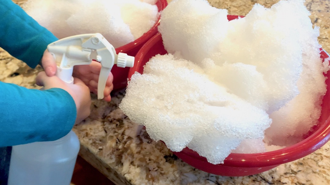 child using a squirt bottle to spray snow in a bowl with warm water