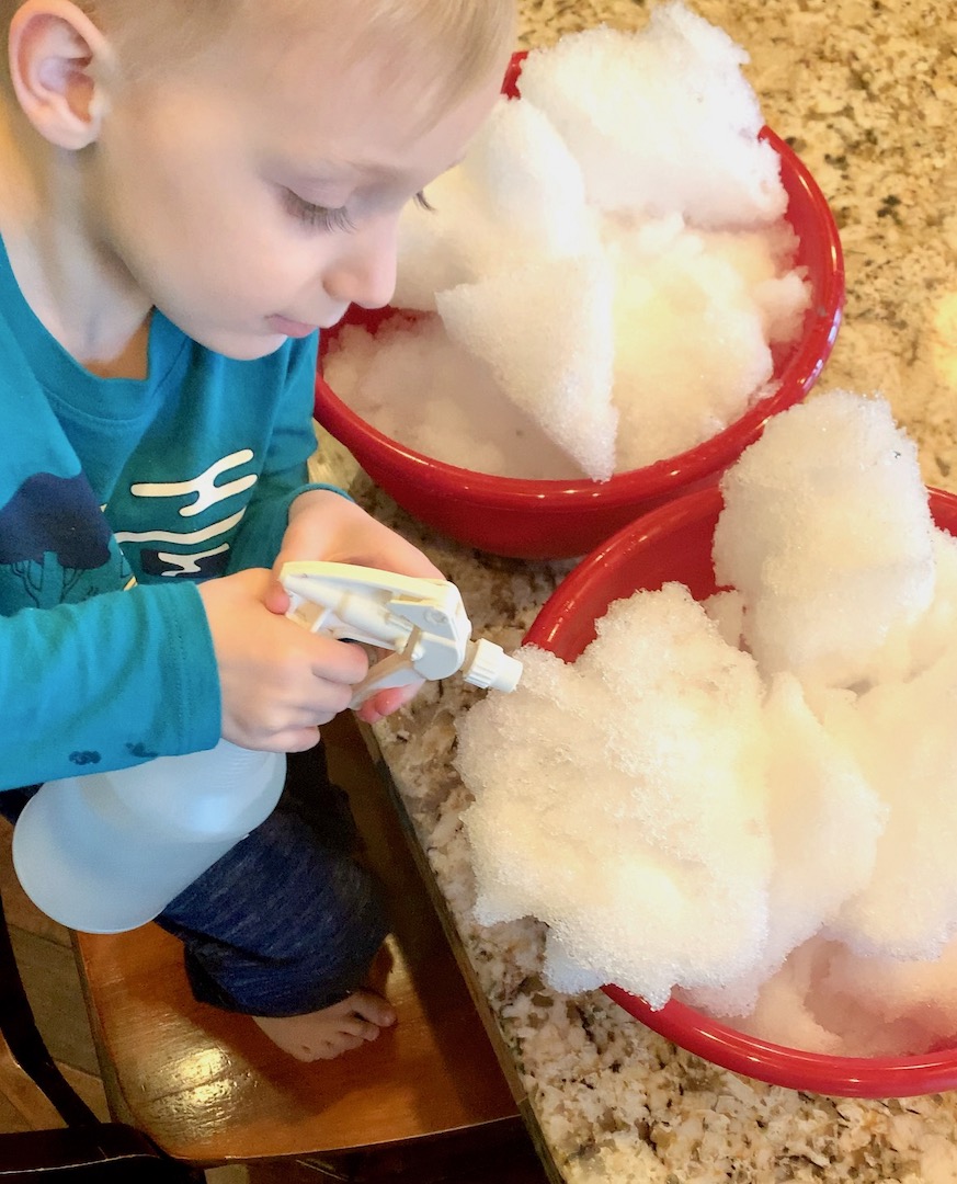 child using a squirt bottle to melt snow in a bowl indoors