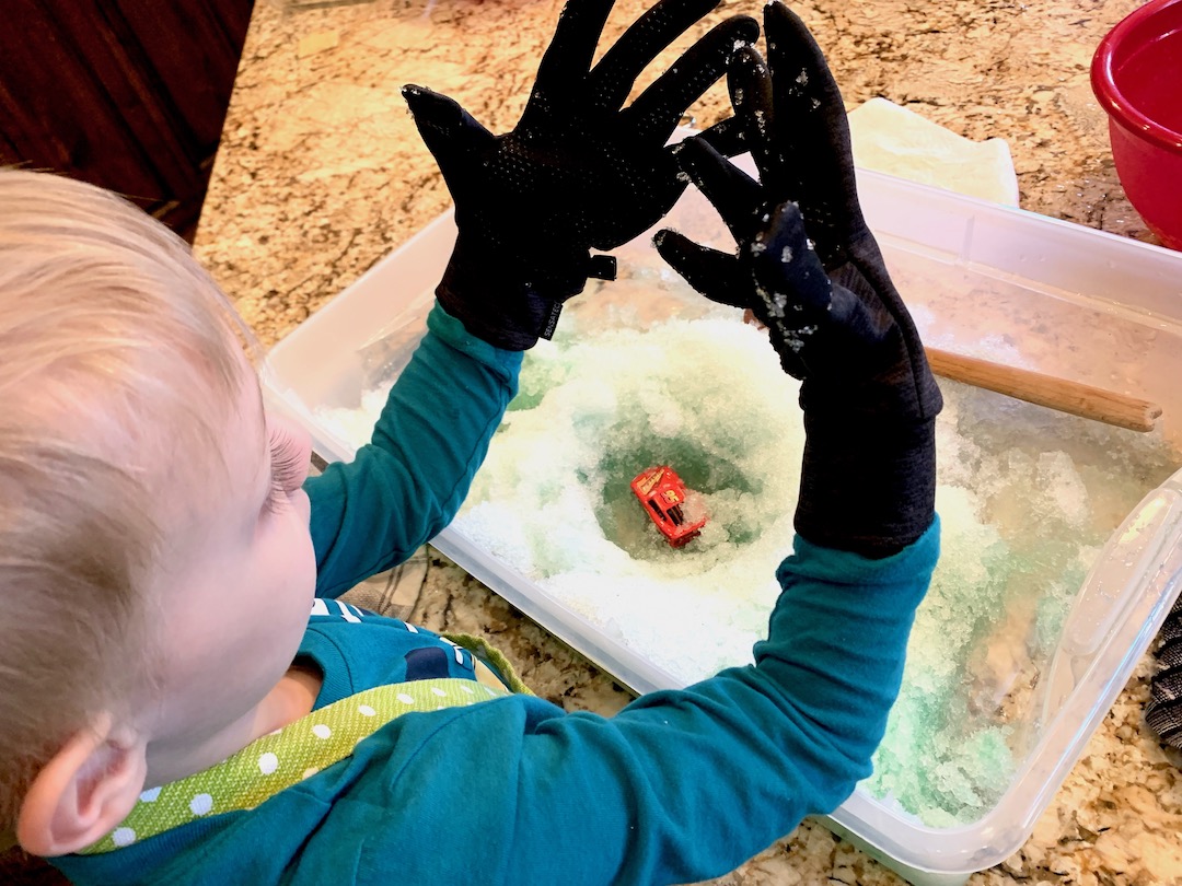 chid playing in a bin of colored snow wearing black gloves