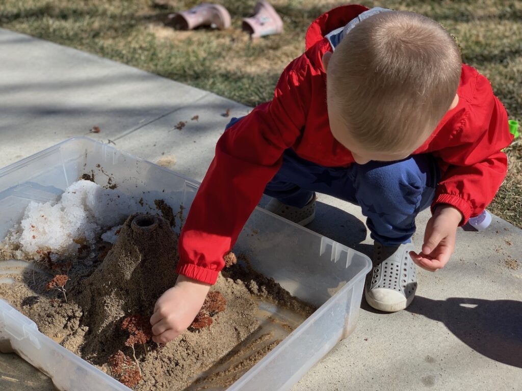 child playing in sand to build a volcano