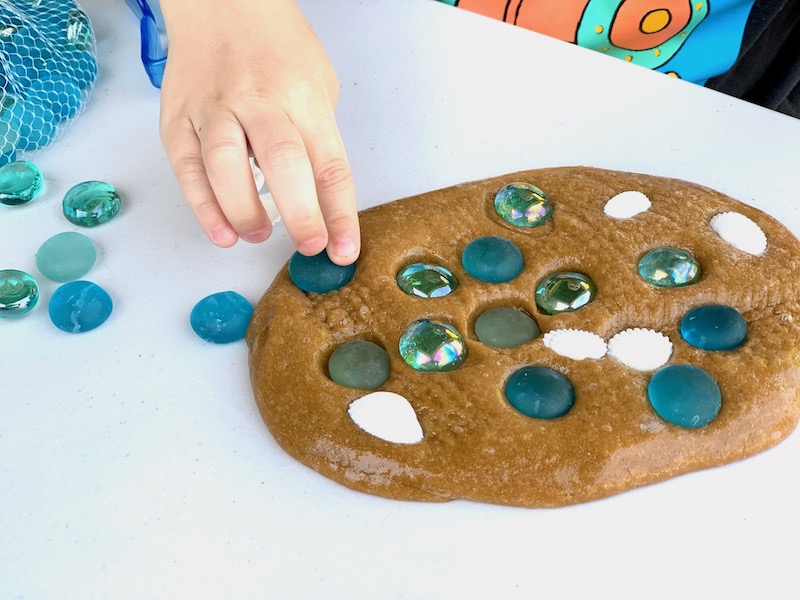 a child's hand pressing colored stones into brown sand slime